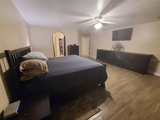 bedroom featuring baseboards, wood finished floors, arched walkways, and ceiling fan