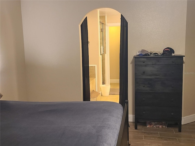 bedroom with arched walkways, connected bathroom, baseboards, and wood finish floors