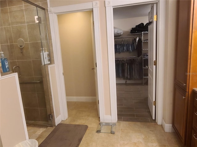 bathroom featuring baseboards, a spacious closet, and a shower stall