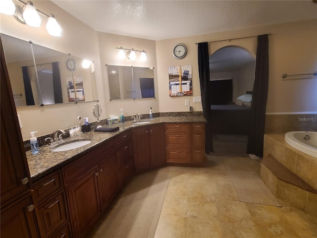 full bathroom with a sink, a relaxing tiled tub, a textured ceiling, and double vanity