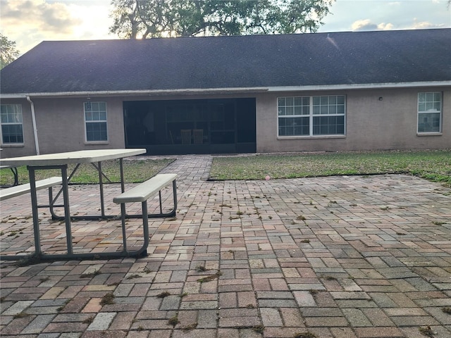 rear view of property featuring a patio area, stucco siding, and a shingled roof