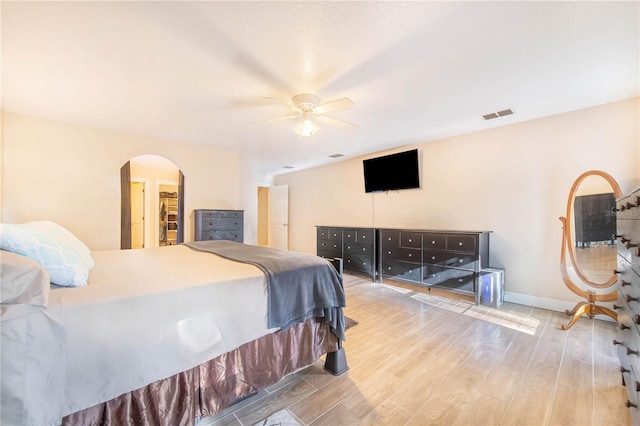 bedroom with baseboards, arched walkways, visible vents, a ceiling fan, and wood finished floors
