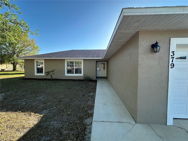 doorway to property with a garage, a shingled roof, a lawn, and stucco siding