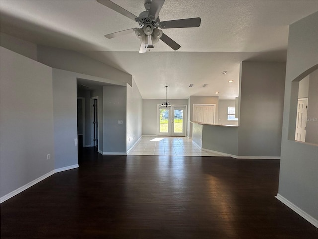 unfurnished living room with a textured ceiling, lofted ceiling, ceiling fan with notable chandelier, wood finished floors, and baseboards