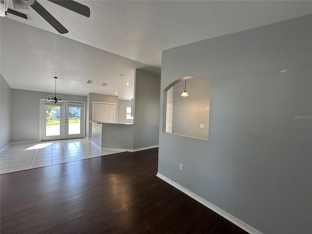 unfurnished living room featuring a textured ceiling, ceiling fan, arched walkways, wood finished floors, and baseboards