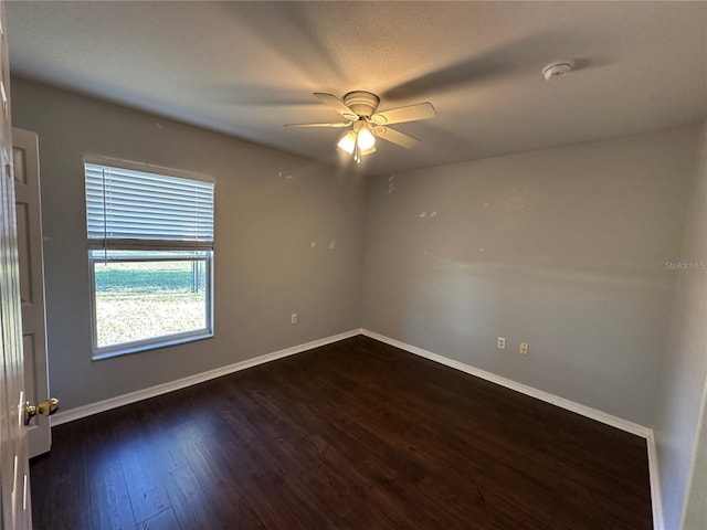 unfurnished room with dark wood finished floors, a ceiling fan, and baseboards