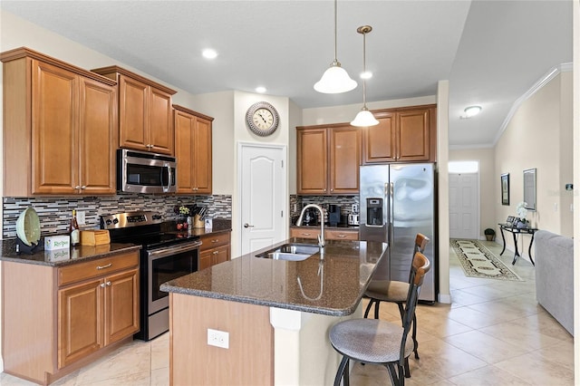 kitchen featuring a breakfast bar, dark stone counters, a sink, appliances with stainless steel finishes, and brown cabinets