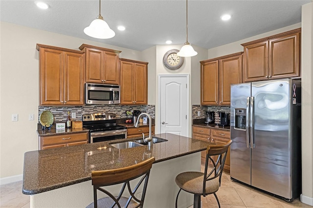 kitchen with a sink, an island with sink, brown cabinetry, and stainless steel appliances