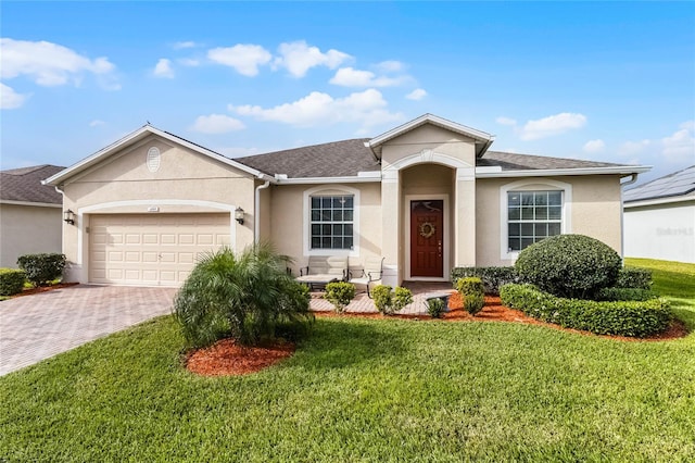 ranch-style home featuring decorative driveway, a front lawn, an attached garage, and stucco siding