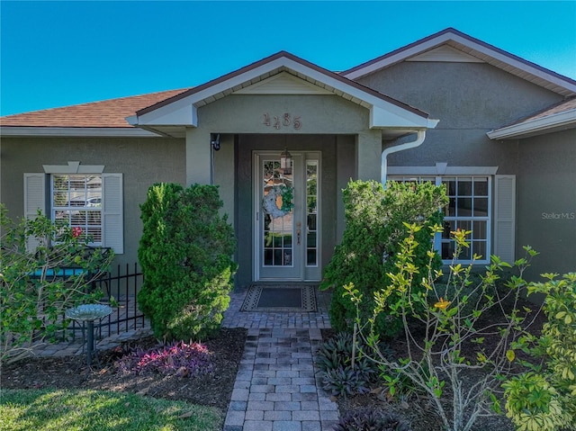 view of exterior entry with a shingled roof and stucco siding