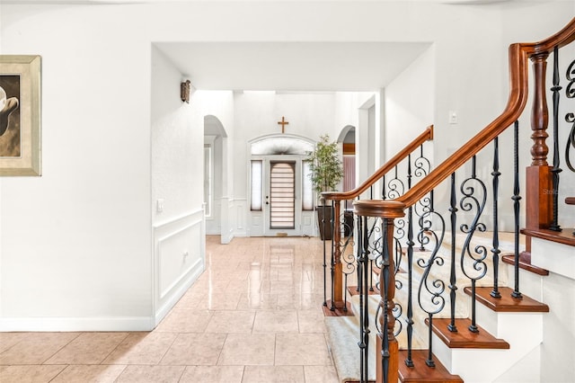 foyer featuring arched walkways, wainscoting, a decorative wall, and light tile patterned floors