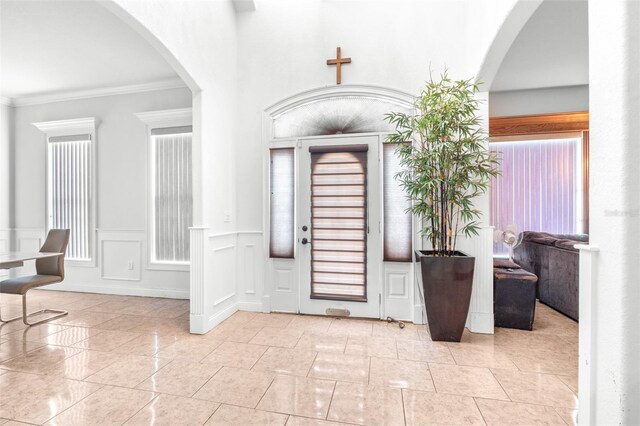 foyer with arched walkways, ornamental molding, wainscoting, and a decorative wall