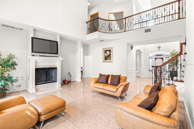 living area featuring visible vents, arched walkways, a towering ceiling, stairs, and a fireplace