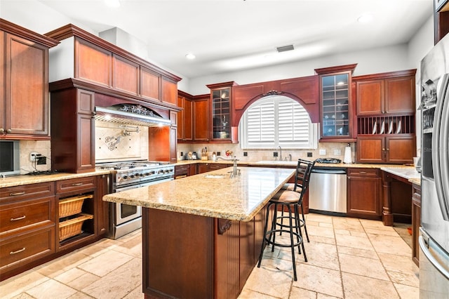 kitchen with light stone counters, stone tile floors, stainless steel appliances, a breakfast bar, and a sink