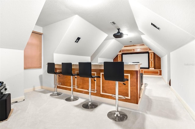 home theater room with a textured ceiling, lofted ceiling, light carpet, visible vents, and baseboards