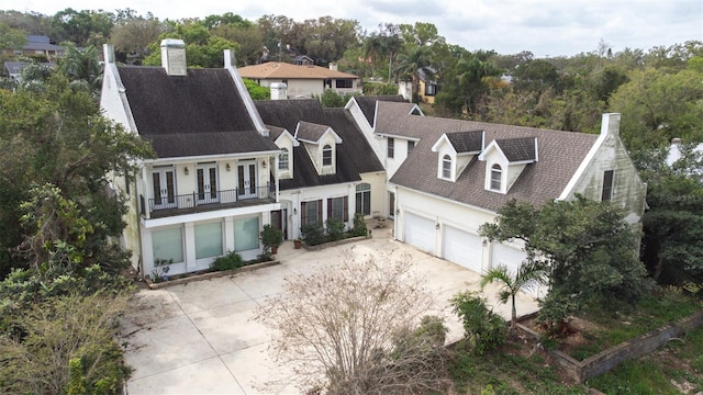 view of front facade with driveway, a garage, a balcony, a chimney, and french doors