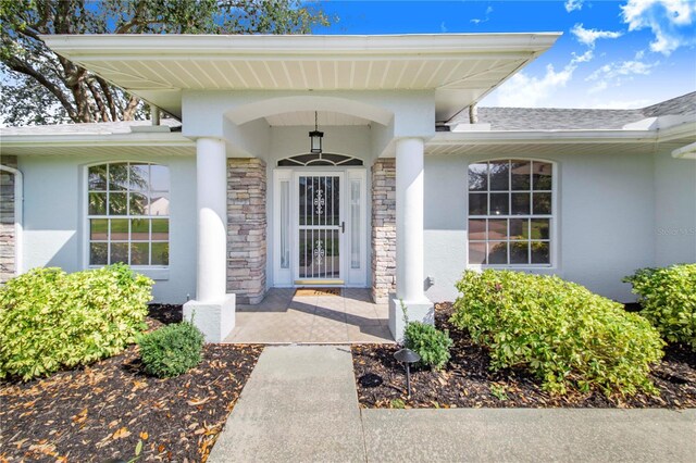 entrance to property featuring stone siding, a shingled roof, and stucco siding