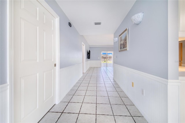 hall with a wainscoted wall, light tile patterned floors, and visible vents