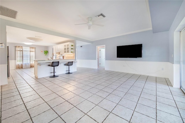 unfurnished living room featuring a ceiling fan, wainscoting, visible vents, and light tile patterned floors