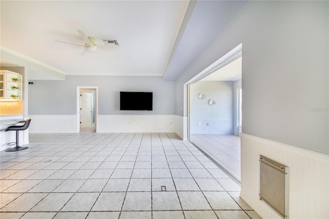 unfurnished living room with light tile patterned floors, visible vents, ornamental molding, wainscoting, and ceiling fan