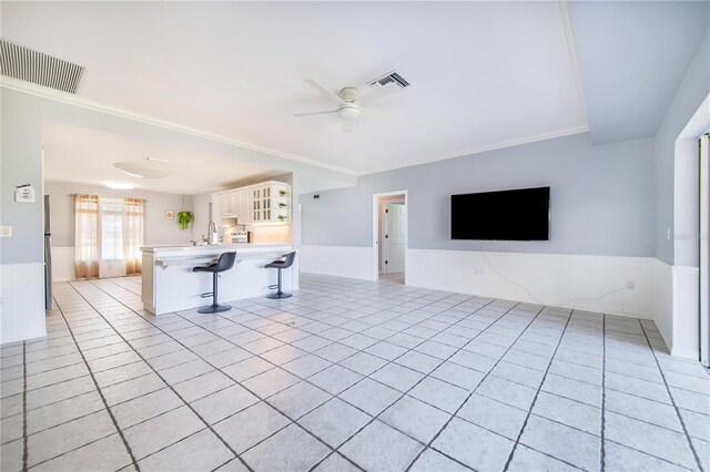 unfurnished living room with light tile patterned floors, crown molding, visible vents, and a ceiling fan