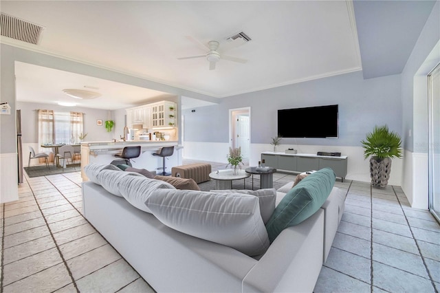 living room featuring ceiling fan, visible vents, crown molding, and wainscoting