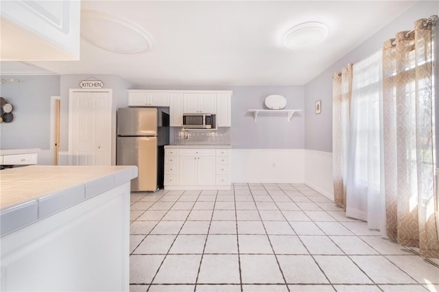 kitchen featuring light tile patterned floors, tile counters, appliances with stainless steel finishes, white cabinetry, and backsplash