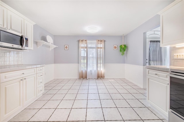 kitchen with tile countertops, stove, white cabinetry, open shelves, and stainless steel microwave