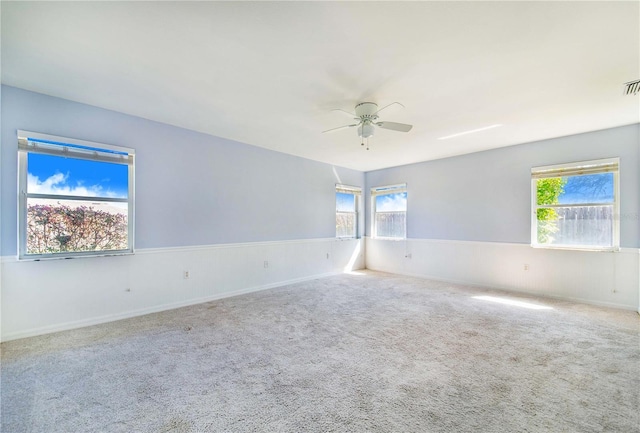 carpeted spare room featuring a wealth of natural light, visible vents, and ceiling fan