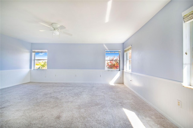 empty room with carpet floors, a wainscoted wall, and a ceiling fan