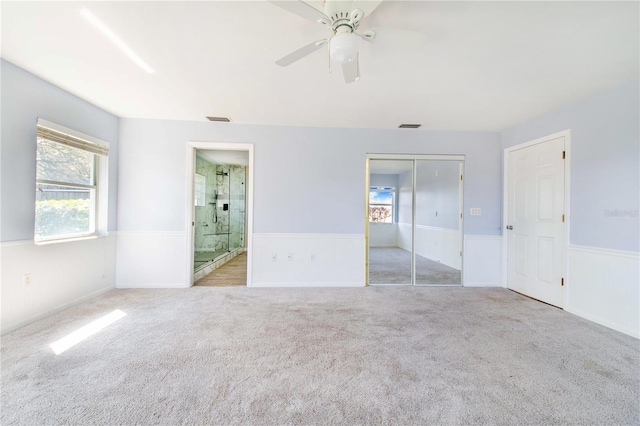 unfurnished bedroom featuring carpet floors, a wainscoted wall, a closet, visible vents, and ensuite bath