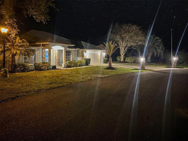 view of front of home with a garage, concrete driveway, a lawn, and stone siding