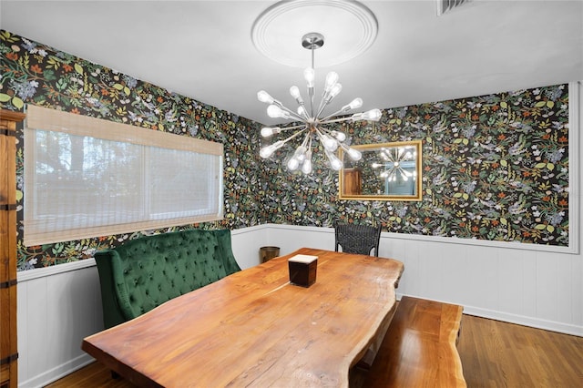 dining room with wallpapered walls, wood finished floors, a wainscoted wall, and a chandelier