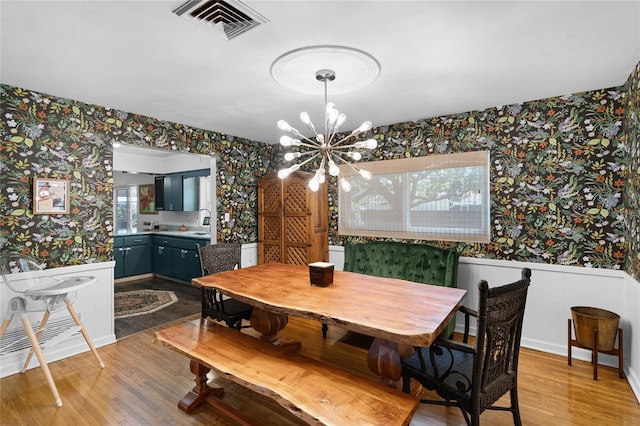 dining room with visible vents, wallpapered walls, light wood-type flooring, wainscoting, and an inviting chandelier