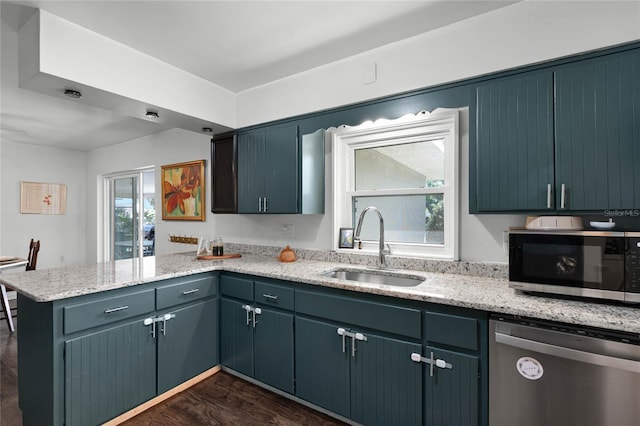 kitchen with dark wood-type flooring, light stone countertops, a peninsula, stainless steel appliances, and a sink