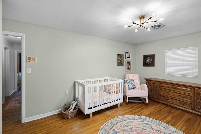 bedroom featuring an inviting chandelier, wood finished floors, visible vents, and baseboards