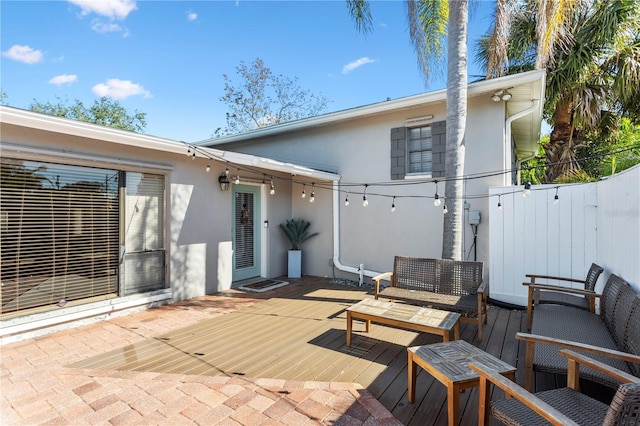 rear view of house with fence, a wooden deck, and stucco siding