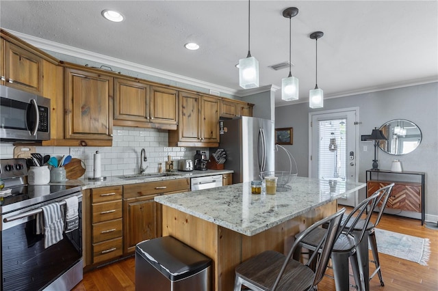 kitchen with a sink, visible vents, appliances with stainless steel finishes, light stone countertops, and brown cabinetry