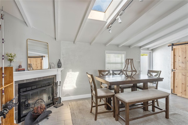 dining area with a barn door, baseboards, beamed ceiling, rail lighting, and a fireplace