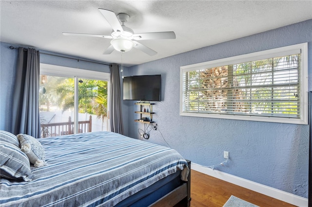 bedroom featuring access to outside, multiple windows, wood finished floors, and a textured wall