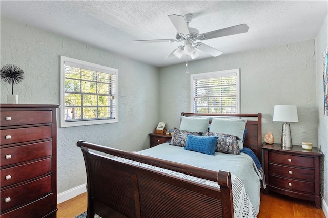 bedroom with a textured wall, a ceiling fan, a textured ceiling, wood finished floors, and baseboards