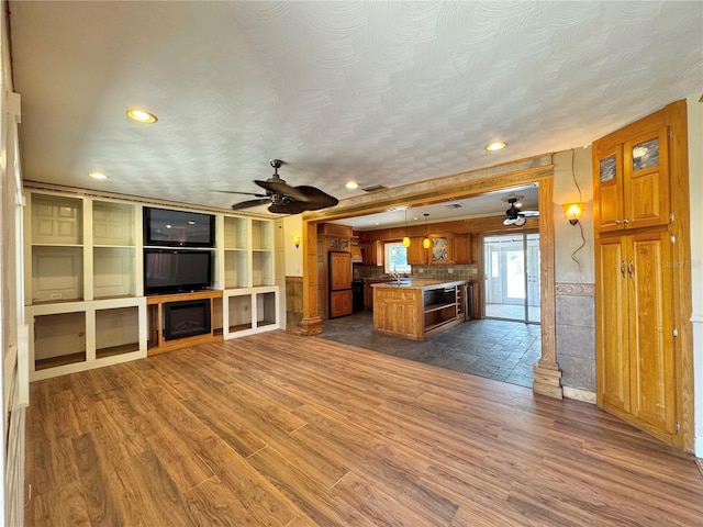 kitchen featuring brown cabinetry, open floor plan, dark wood finished floors, and a ceiling fan