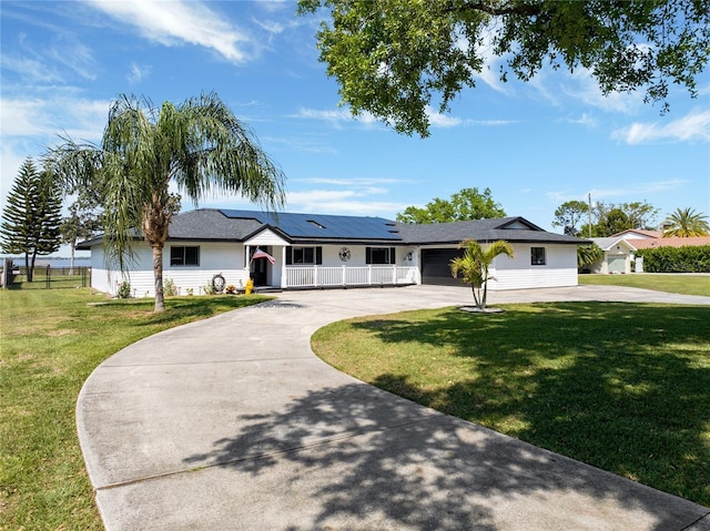 ranch-style home with roof mounted solar panels, covered porch, driveway, and a front lawn