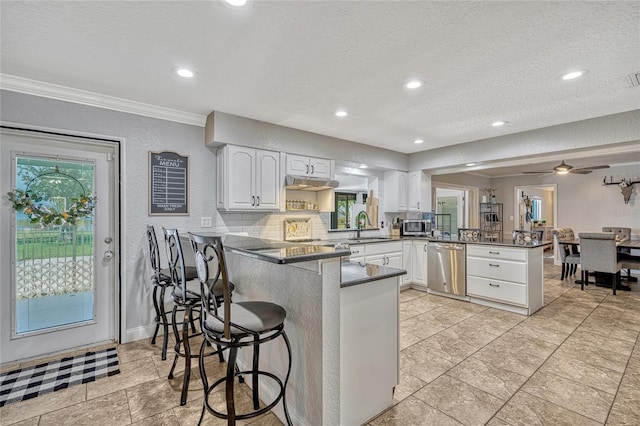 kitchen featuring a peninsula, a sink, appliances with stainless steel finishes, white cabinetry, and dark countertops