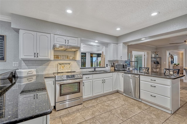 kitchen with under cabinet range hood, a peninsula, a textured wall, stainless steel appliances, and a sink