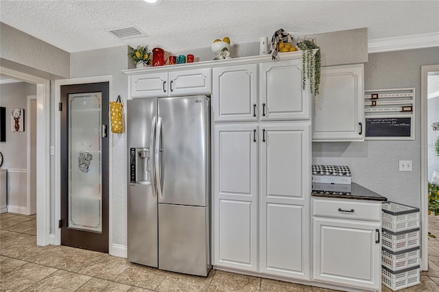 kitchen with dark countertops, visible vents, white cabinetry, stainless steel fridge, and a textured ceiling