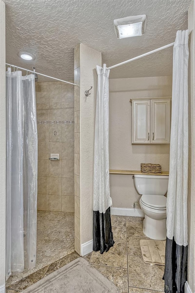 bathroom with tiled shower, toilet, and a textured ceiling