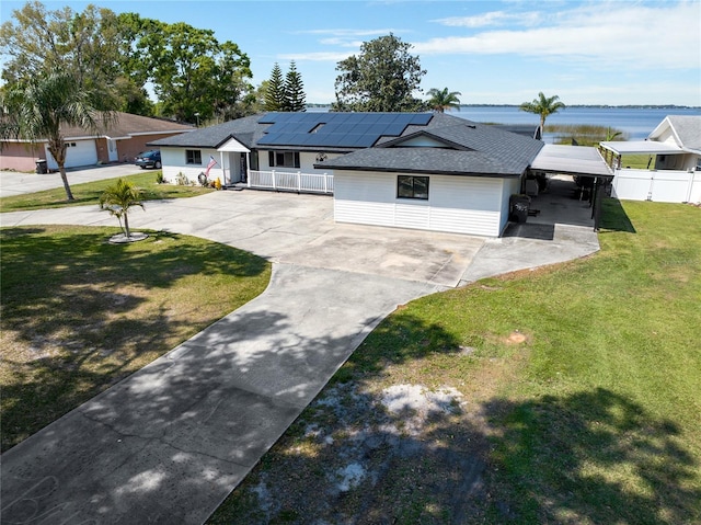 view of front of house featuring a front lawn, a water view, fence, concrete driveway, and roof mounted solar panels