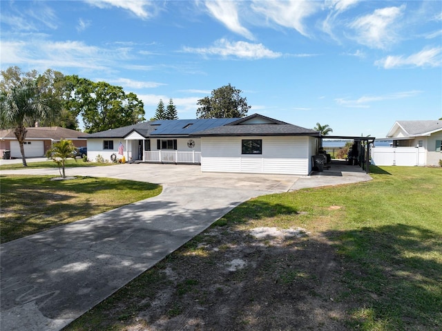 ranch-style home with a front yard, fence, driveway, and roof mounted solar panels