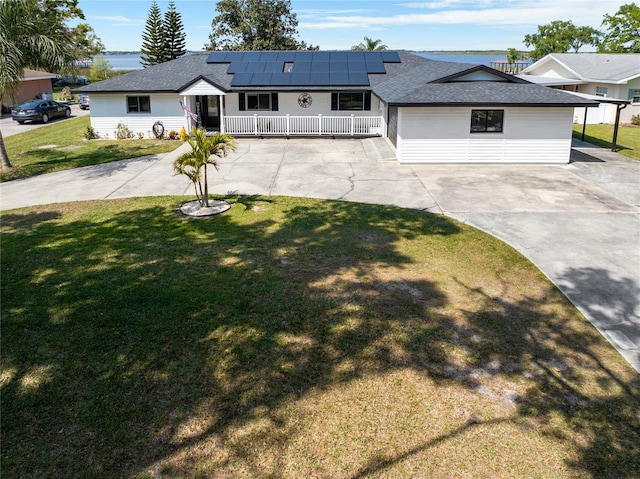 view of front of property featuring driveway, covered porch, a shingled roof, a front lawn, and roof mounted solar panels